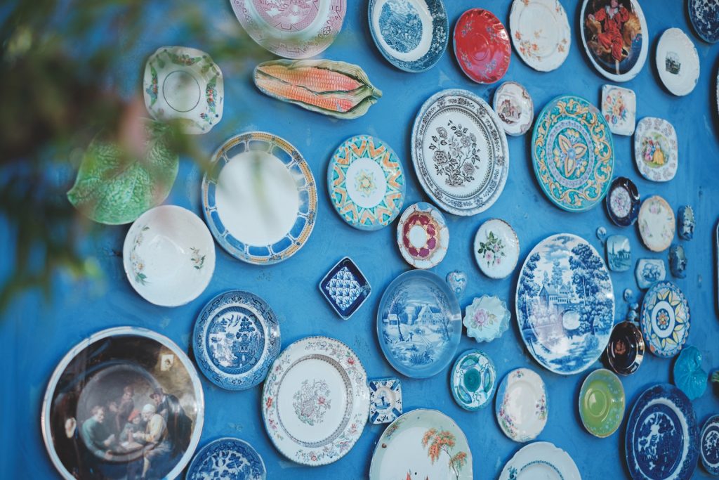 Collection of various ceramic plates of different sizes and ornaments arranged on bright blue wall in studio